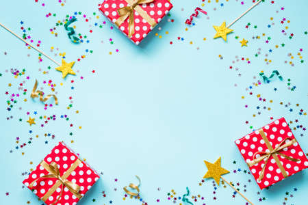 Top view of a red dotted gift boxes, golden magic wands, colorful confetti and ribbons over blue background. Celebration concept. Copy space.の写真素材