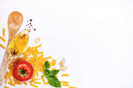 Top view of pasta ingredients over white background - raw fusilli, fresh basil, garlic cloves, olive oil and ripe tomatoe. Italian food concept. Copy space.の写真素材