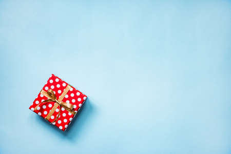 Top view of a red dotted gift box tied with golden bow over blue background. Copy space.の写真素材