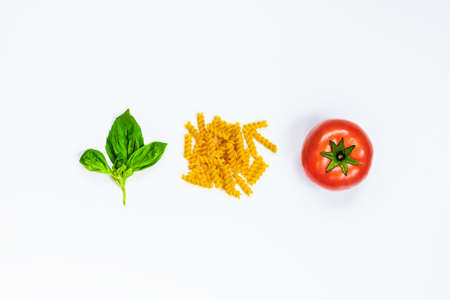 Top view of pasta ingredients over white background - raw fusilli, fresh basil and ripe tomatoe....