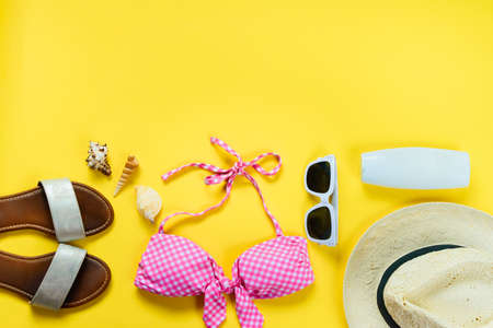 Top view of two pieces pink swimming suit and beach accessoties over yellow background.の写真素材