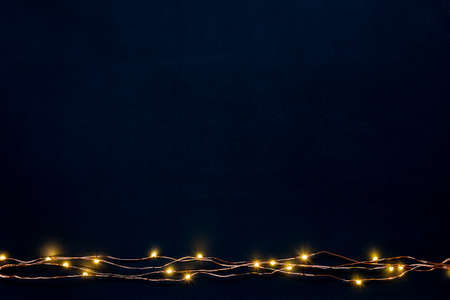 Christmas lights garland border over black background. Flat lay, copy space.