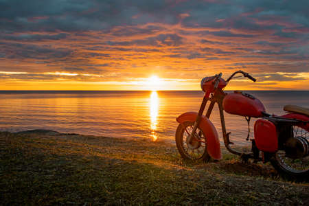 A skeleton of an old red motorcycle against the picturesque sunrise.の写真素材