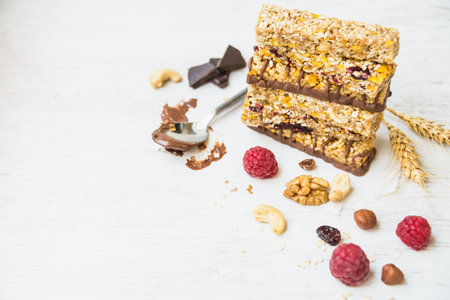 A pile of various homemade granola bars with nuts, seeds, dark chocolate, honey and berries over a white background. Copy space.の写真素材
