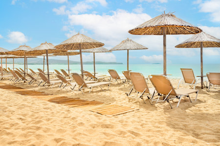Straw umbrellas and sunbeds on a sunny golden tropical beach seashore.の写真素材