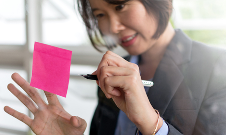 Asian business woman write on post it stic on transparent wall in brainstorm or planning workの写真素材