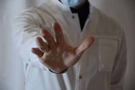Soft focus of unrecognizable young male doctor in white medical coat outstretching palm while...