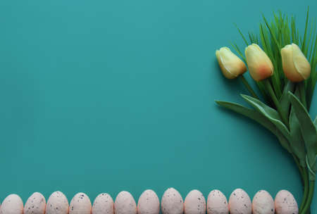 Overhead view of tulips and row of small artificial oval eggs covered with dark brown spots on vibrant turquoise backgroundの写真素材