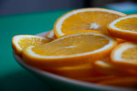 Selective focus closeup of vibrant big round thin slices of orange on round plate on dark green table in daytime on blurred backgroundの写真素材