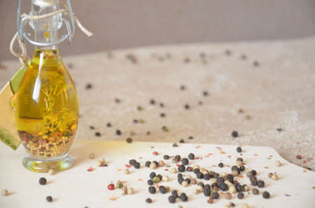 A glass jar with olive oil and spices and sprinkled with pepper on a table and cutting board