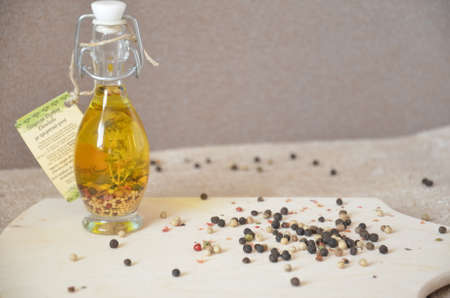 A glass jar with olive oil and spices and sprinkled with pepper on a table and cutting boardの写真素材