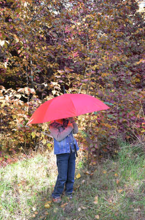 handsome cute boy with brown eyes in a jeans jacket in the autumn park with a red umbrella,の写真素材