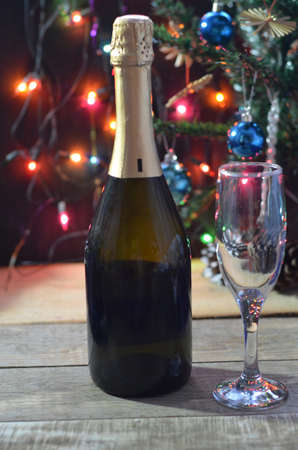 a bottle of champagne and glasses on the background of a Christmas tree decorated with balls and New Year's lights. happy christmas concept Ribbon, baubles and wine against Christmas lightsの写真素材