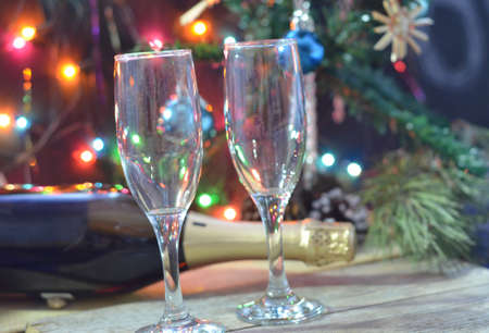 a bottle of champagne and glasses on the background of a Christmas tree decorated with balls and New Year's lights. happy christmas concept Ribbon, baubles and wine against Christmas lightsの写真素材