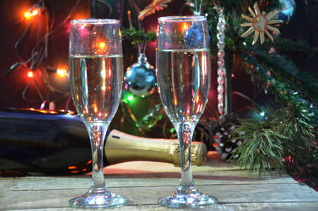 a bottle of champagne and glasses on the background of a Christmas tree decorated with balls and New Years lights. happy christmas concept. Ribbon, baubles and wine against Christmas lightsの写真素材