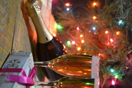 two glasses of champagne on the background of champagne. Christmas tree with Christmas lights. New Year and Christmas, Gift boxes tied with bowsの写真素材