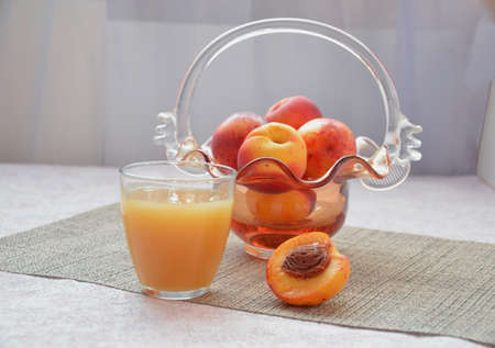 Ripe peaches and glass of juice on a table, cut peach, of a beautiful vase in the shape of a basket backgroundの写真素材