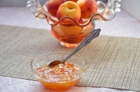Bowl of peach jam on on a table, cut peach on a plate, of a beautiful vase in the shape of a basket backgroundの写真素材