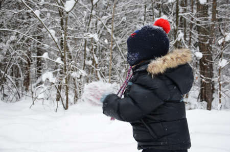 A simpotic little boy throws snow in the winter snow-covered forest, trees in the snow. enjoys the winter. plays snowballs. happy, smiling, laughing with falling snowの写真素材