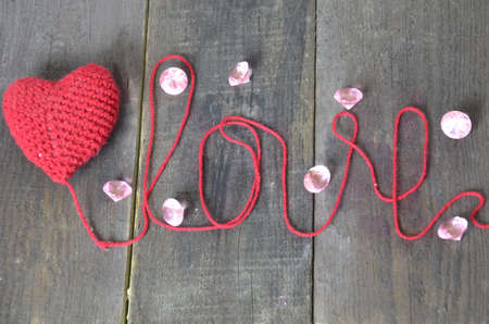 Close up red hand-made knitting crochet heart with diamonds, crystals on wooden background. Love and...