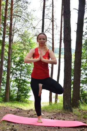 beautiful young girl walking in forest standing on log in yoga tree poseの写真素材