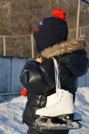 cute little boy wearing warm winter clothes going ice skating. skates for figure skating. skating rink on the street. enjoys winter. Winter sportsの写真素材