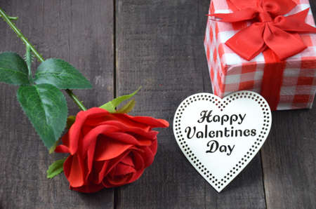Gift or present box with red bow ribbon and a wooden heart with the inscription of a happy Valentine's day on wooden table for Valentines dayの写真素材