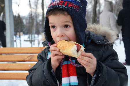 A boy eating a hot dog outdoors winterの写真素材