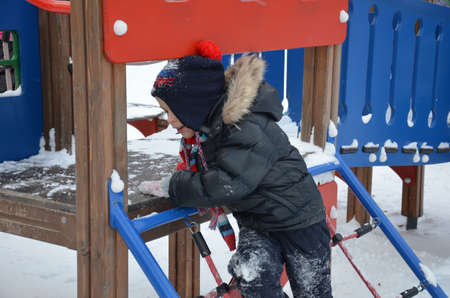 closeup portrait of happy laughing children boy in winter clothes outside playing in the snow drifts on the bright colorful playground in the winterの写真素材