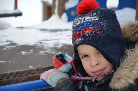 closeup portrait of happy laughing children boy in winter clothes outside playing in the snow drifts on the bright colorful playground in the winterの写真素材