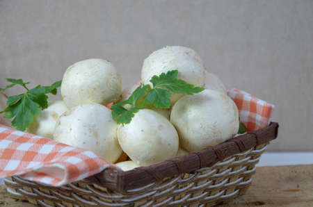 Fresh white mushrooms champignon in brown basket on wooden background. Top view. Copy space.の写真素材
