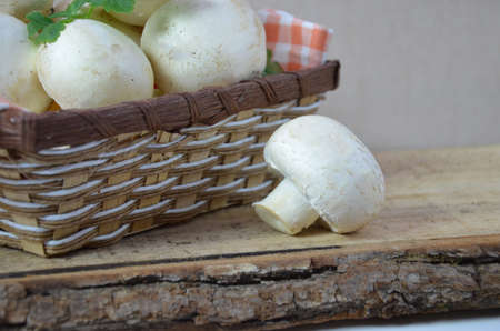 Fresh white mushrooms champignon in brown basket on wooden background. Top view. Copy space.の写真素材