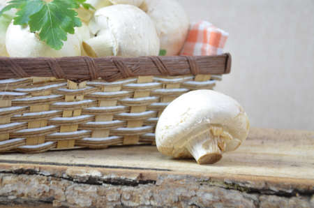 Fresh white mushrooms champignon in brown basket on wooden background. Top view. Copy space.の写真素材