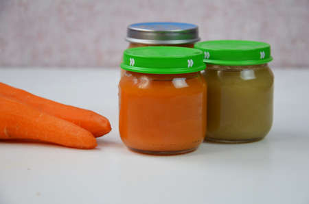 baby mashed with spoon in glass jar on white backgroundの写真素材