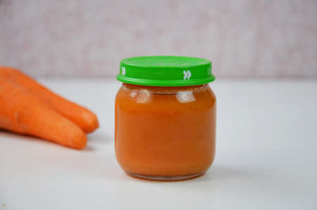baby mashed with spoon in glass jar on white backgroundの写真素材