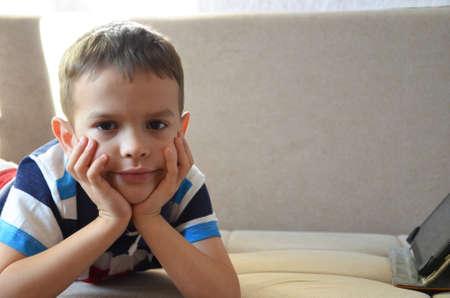Tired young boy with glasses sitting and holding his head on the tablet in front of the computer, tablet and laptopの写真素材