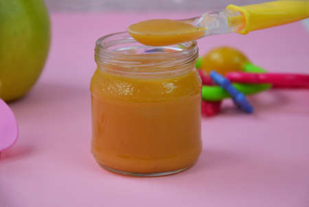 Fresh, organic pureed fruits for baby. mashed green apple. homemade, organic, healthy baby foods. on pink background. baby spoonの写真素材