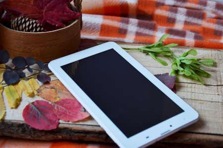 a white tablet computer with a blank screen on a wooden table with autumn leaves, ginger cookie red maple leaf, cup of coffee to go, top viewの写真素材