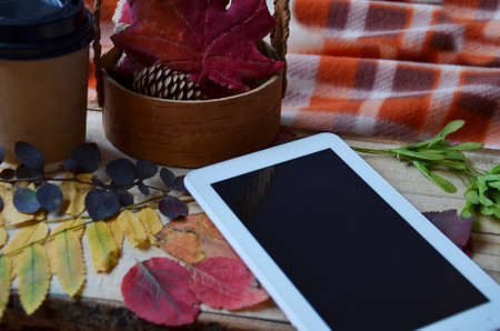 a white tablet computer with a blank screen on a wooden table with autumn leaves, ginger cookie red maple leaf, cup of coffee to go, top viewの写真素材