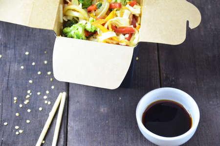 Chinese or korean food noodles on sticks. in the card box take out or to go. soy sauce. with vegetables on a wooden tableの写真素材