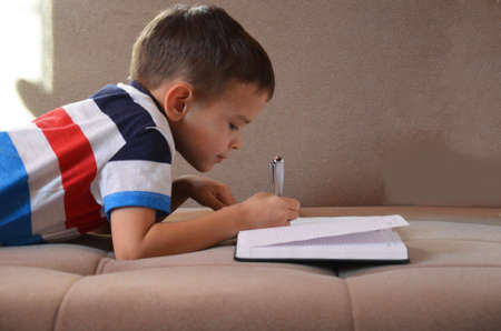 Close up little boy hand writing on paper, Kid writing on sofa in living room, student child boy holding colour pencil learning how to write homework at home, education conceptの写真素材
