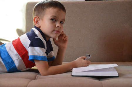 Close up little boy hand writing on paper, Kid writing on sofa in living room, student child boy holding colour pencil learning how to write homework at home, education conceptの写真素材