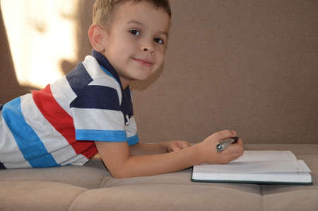 Close up little boy hand writing on paper, Kid writing on sofa in living room, student child boy holding colour pencil learning how to write homework at home, education conceptの写真素材