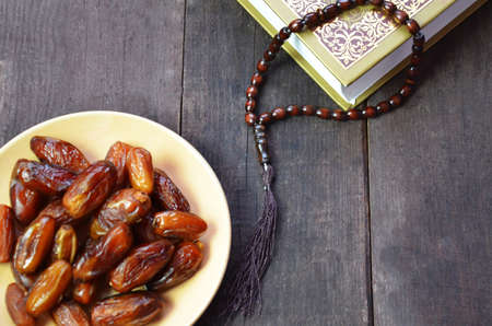 Silver bowl full of dry dates, glass of water for iftar and prayer rosary beads with holy Koran on black background. Ramadan month. Islamic religion concept.の写真素材