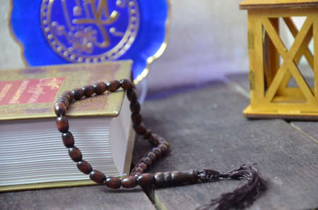 Quran, beads, and lantern on old wood with a beautiful sunrise as background. Ramadhan Concept.