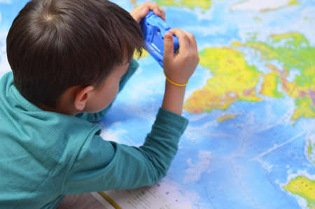 handsome boy in vivid yellow shirt with film retro camera in hands on world map backgroundの写真素材