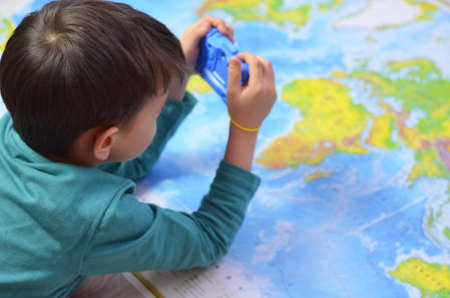 handsome boy in vivid yellow shirt with film retro camera in hands on world map backgroundの写真素材