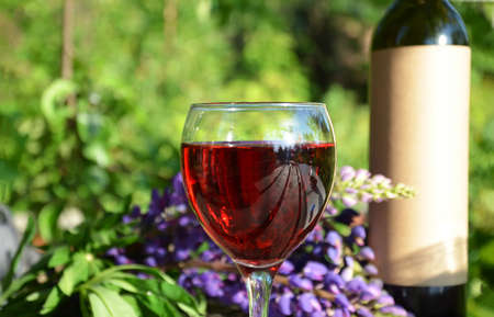 Red wine poured into wine glass on background of green tree leaf foliage. purpie flowerの写真素材