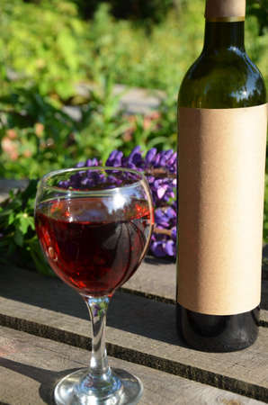 Red wine poured into wine glass on background of green tree leaf foliage. purpie flowerの写真素材