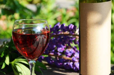Red wine poured into wine glass on background of green tree leaf foliage. purpie flowerの写真素材